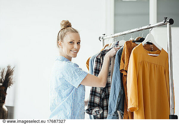 Smiling fashion designer arranging clothes in rack at studio