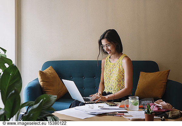 Smiling fashion designer sitting on couch using laptop