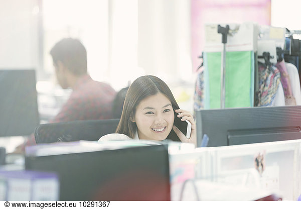 Smiling fashion designer talking on cell phone at desk in office
