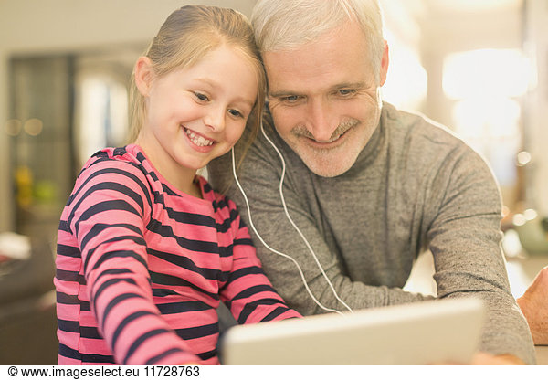 Smiling father and daughter sharing headphones  watching video on digital tablet
