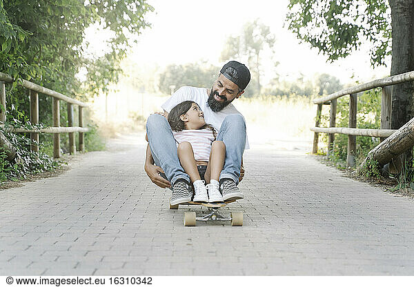 Smiling father and daughter skateboarding on footpath at park