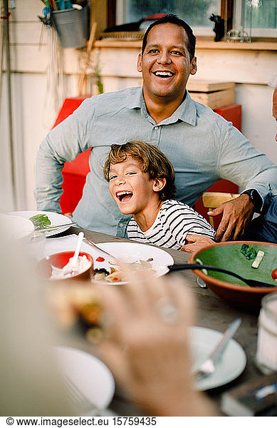 Smiling father and son sitting at dining table during family lunch