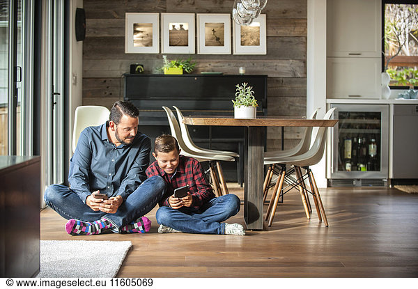Smiling father and son sitting on floor texting on cell phones
