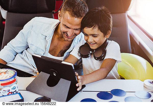 Smiling father and son using digital tablet while sitting in train