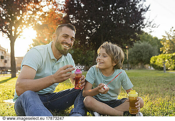 Smiling father and son with bubble wands sitting at park