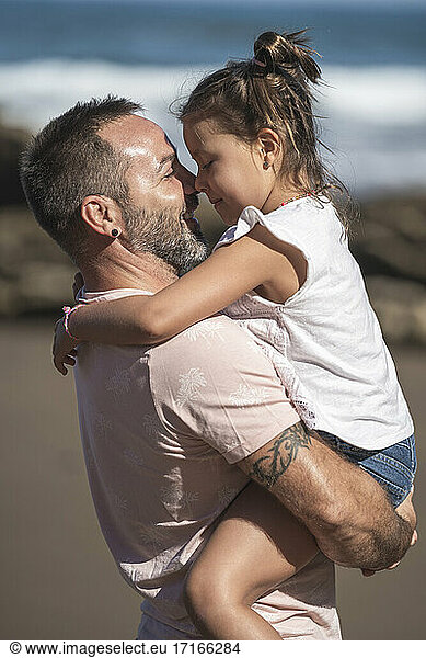 Smiling father carrying daughter at beach during sunny day
