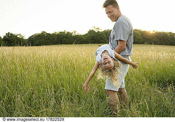 Smiling father carrying daughter enjoying at field