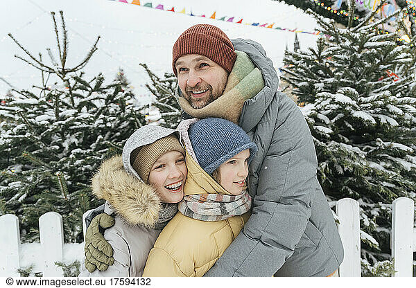 Smiling father embracing children in warm clothing at backyard
