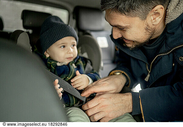 Smiling father fastening car seat belt for son
