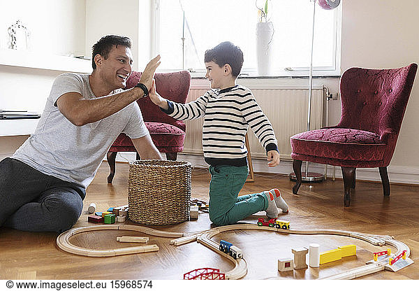 Smiling father giving high-five to son while sitting with toys in living room
