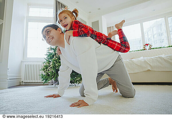 Smiling father giving piggyback ride to daughter on carpet at home