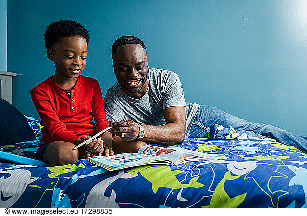 Smiling father helping smiling son with homework on the bed at home