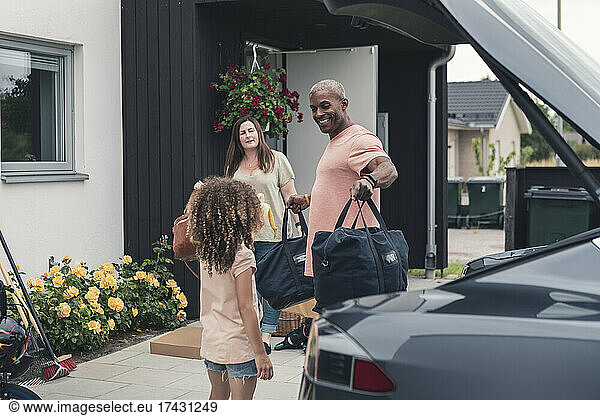 Smiling father looking at daughter while loading luggage in electric car