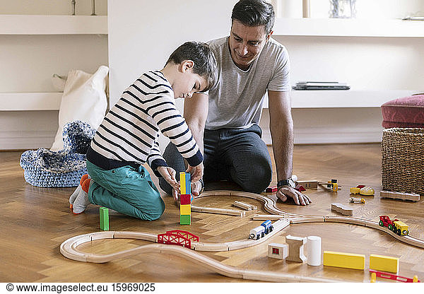 Smiling father playing with son while kneeling in living room