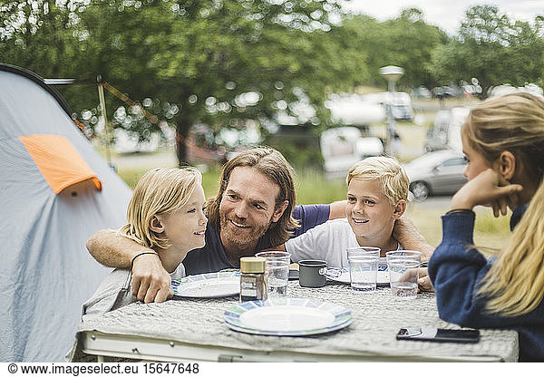 Smiling father sitting with children at table in camping site