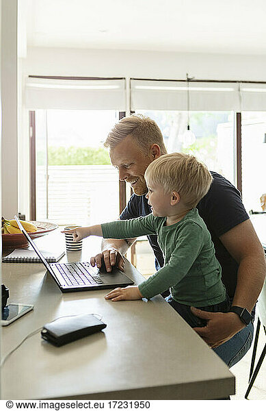 Smiling father using laptop while sitting with son at home