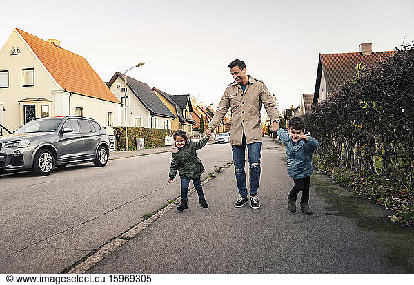 Smiling father walking with children on sidewalk during autumn