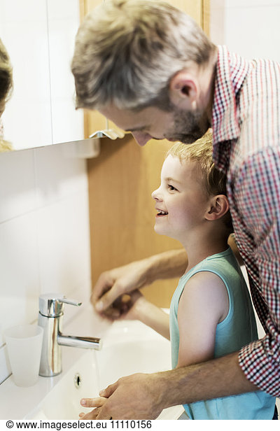 Smiling father washing boy's hands in sink at home