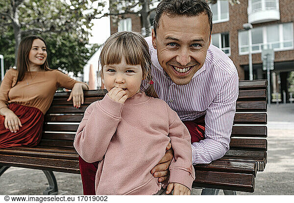 Smiling father with daughter and girlfriend on park bench