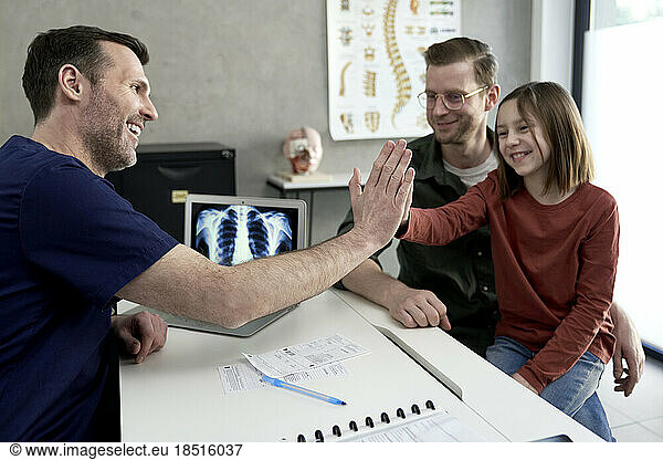 Smiling father with daughter giving high-five to doctor