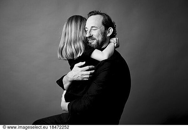 Smiling father with eyes closed embracing daughter