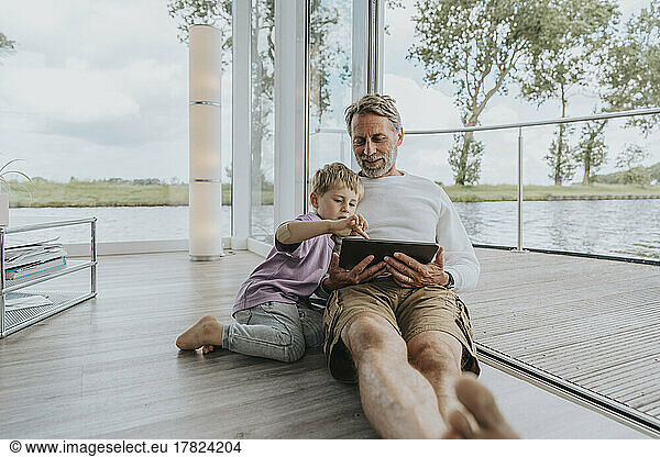 Smiling father with son using tablet PC sitting on floor