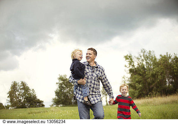 Smiling father with sons on grassy field against sky