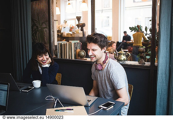 Smiling female and male creative professionals discussing over laptop at desk in office