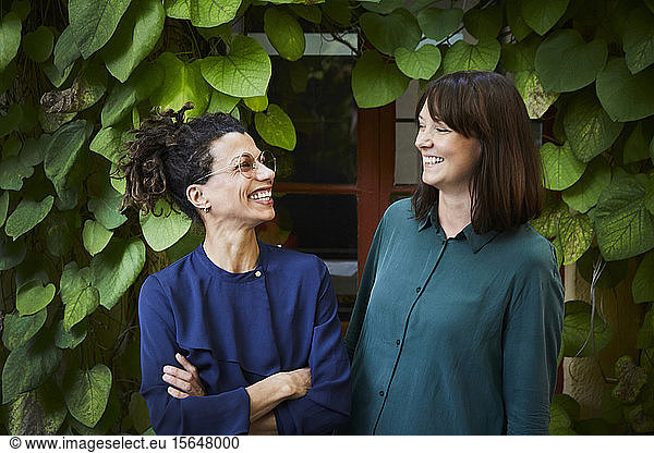 Smiling female architects against creeper plants in backyard