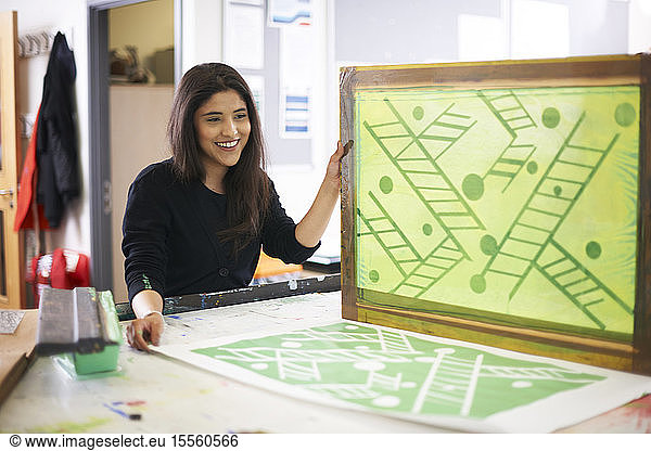 Smiling female art student screen printing in art studio