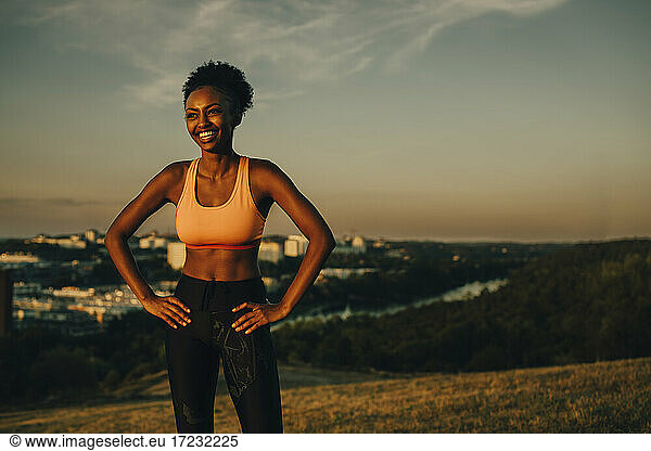 Smiling female athlete with hand on hip during sunset