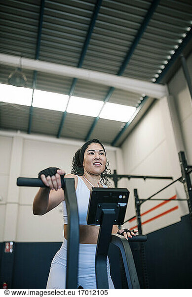 Smiling female athlete working out on exercise machine in gym