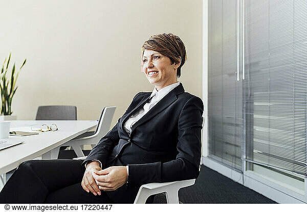 Smiling female business professional day dreaming while sitting on chair in office