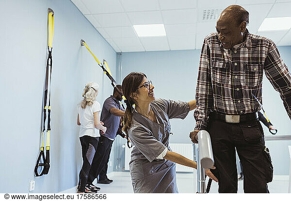 Smiling female caregiver helping senior man to walk at nursing home