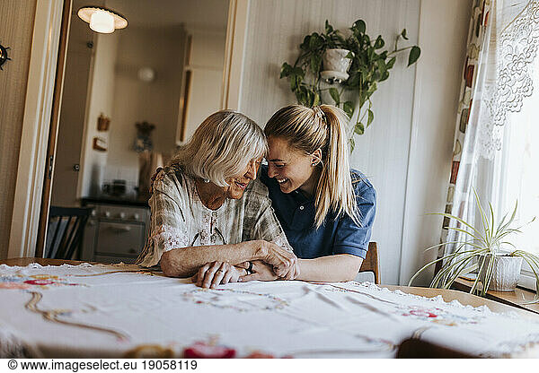 Smiling female caregiver spending leisure time with senior woman sitting at home