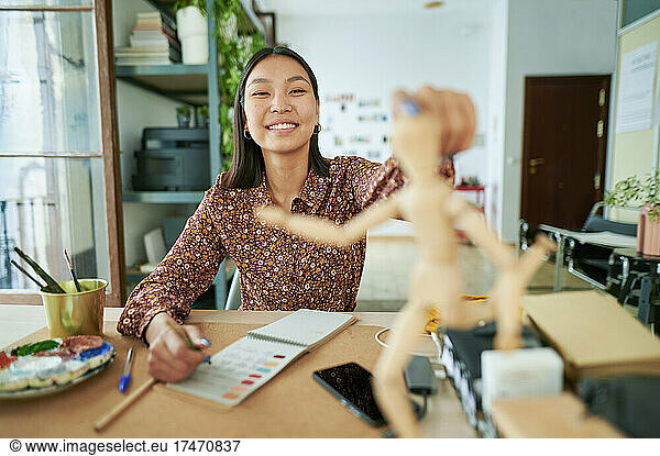 Smiling female cartoonist looking at figurine on desk