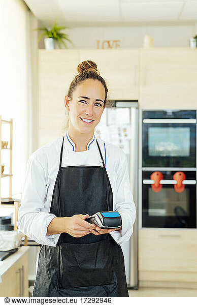 Smiling female chef holding credit card reader in restaurant