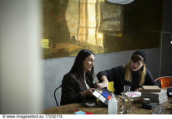 Smiling female colleagues choosing color from swatches during meeting in office
