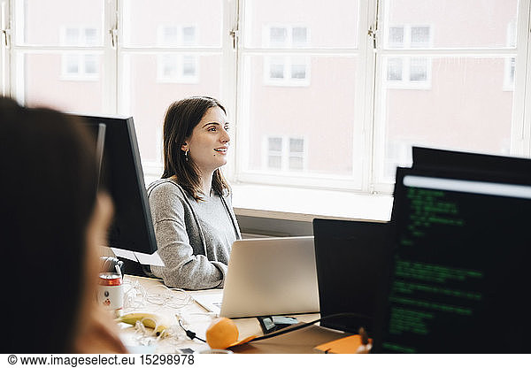 Smiling female computer programmer looking away while sitting at desk in office