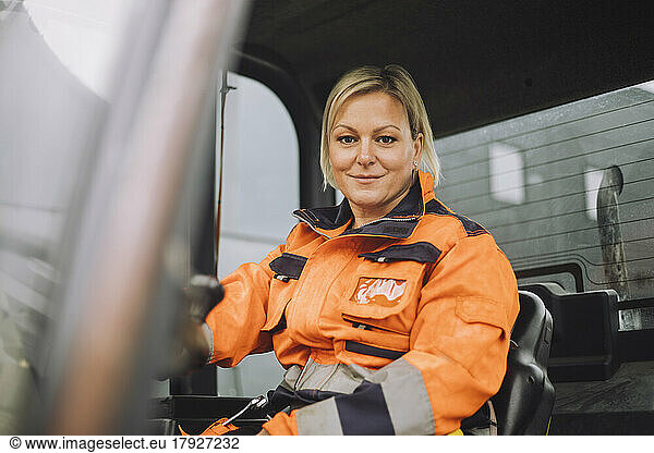 Smiling female construction worker in reflective clothing sitting in vehicle