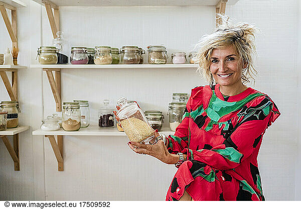 Smiling female cook holding spice container while sitting in cooking class
