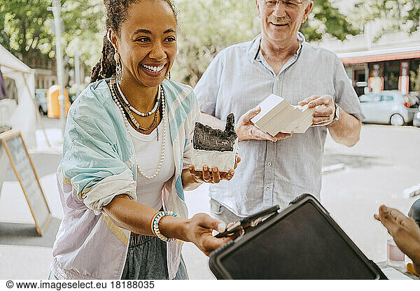 Smiling female customer holding house model while doing mobile payment at flea market