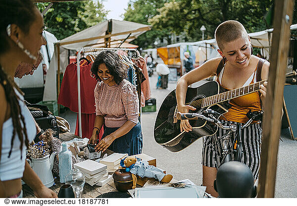 Smiling female customer playing guitar while shopping at flea market
