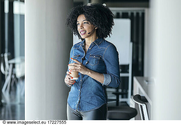 Smiling female customer service representative looking away while having coffee in office