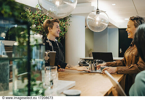 Smiling female customer talking with businesswoman in coffee shop