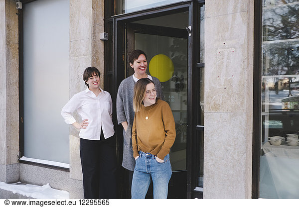 Smiling female design professionals standing at entrance of workshop