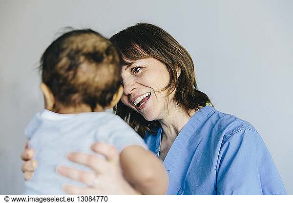 Smiling female doctor carrying baby boy while standing against white background