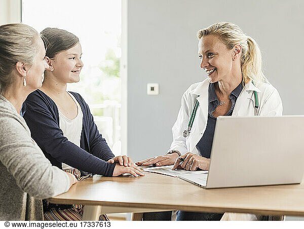 Smiling female doctor looking at girl sitting with mother in office
