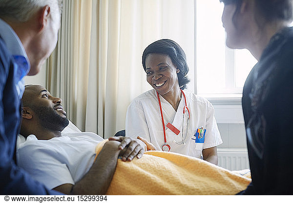 Smiling female doctor talking to patient and family in hospital ward