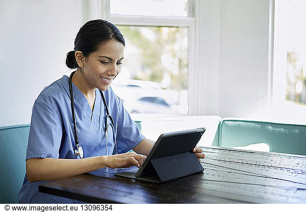 Smiling female doctor using tablet computer at table in hospital